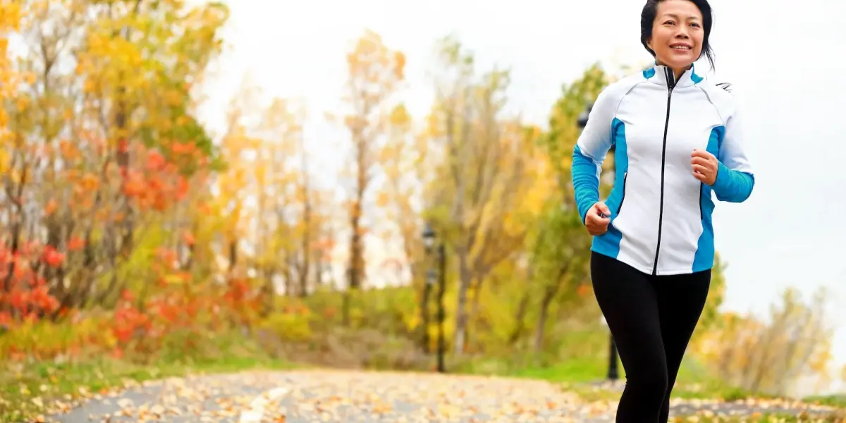 Woman jogging outdoors on an autumn path surrounded by colourful trees