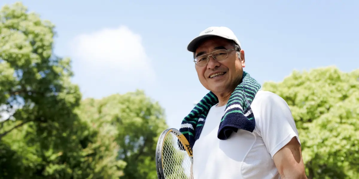 Older man holding a tennis racket outdoors after exercise